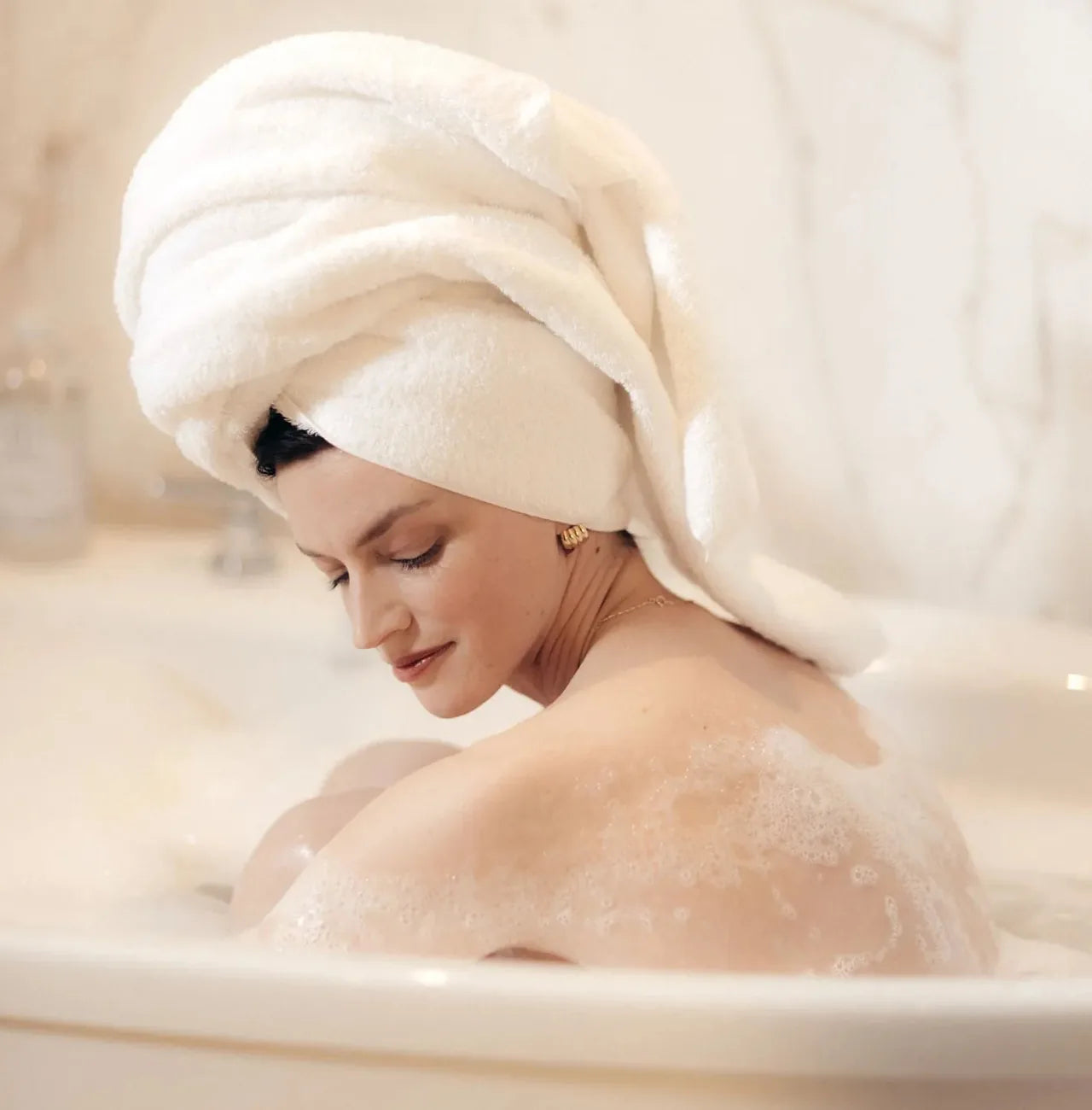 A woman resting in a milky Bathorium bath, hair wrapped in a towel