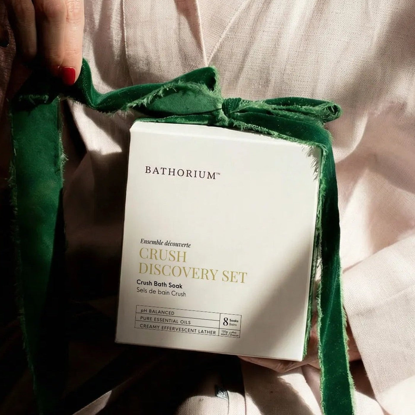 A woman in a robe holding the Bathorium Crush Discovery Set, tied with a green ribbon