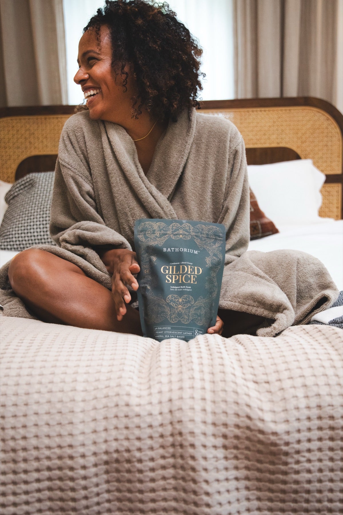 Sitting on the bed in a robe, holding the Gilded Spice pouch