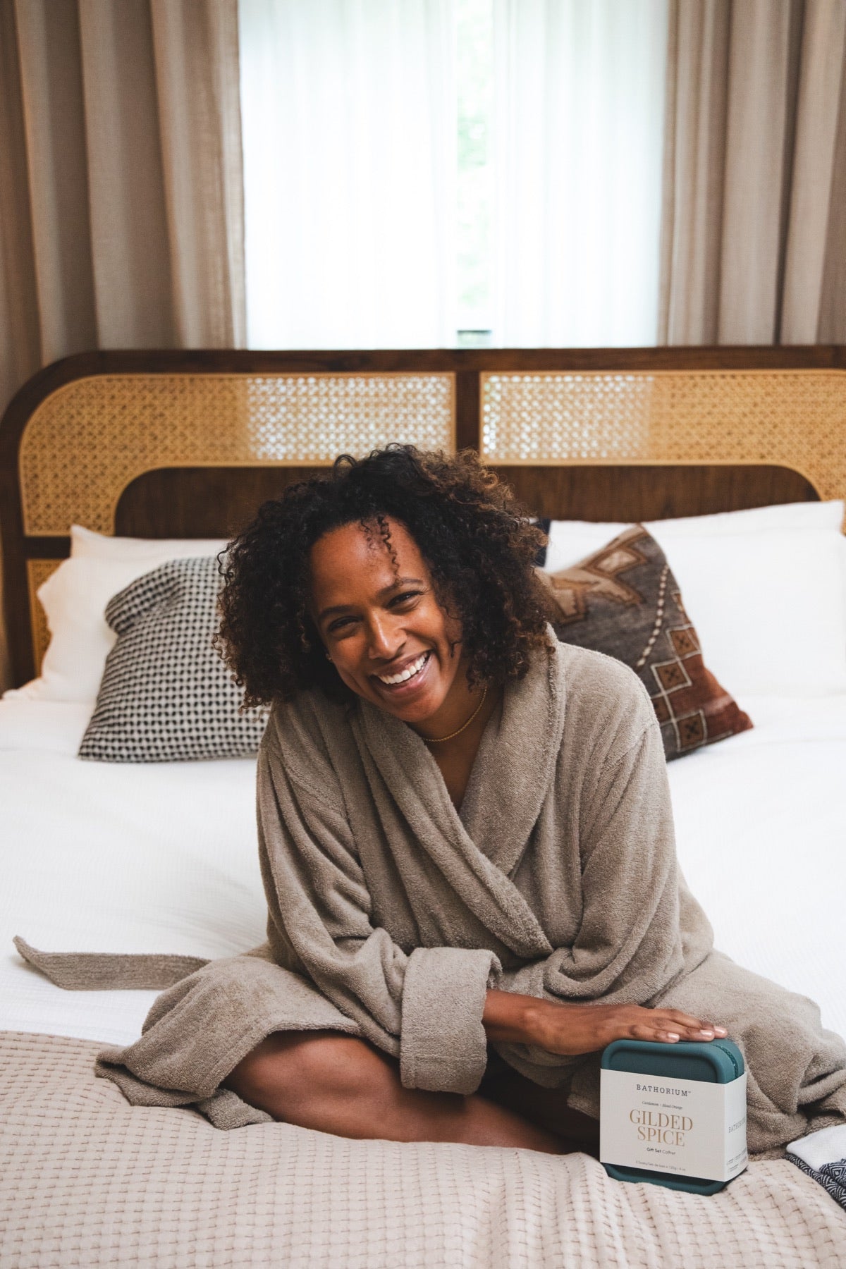 Laughing on the bed in a robe with the Gilded Spice Travel Kit