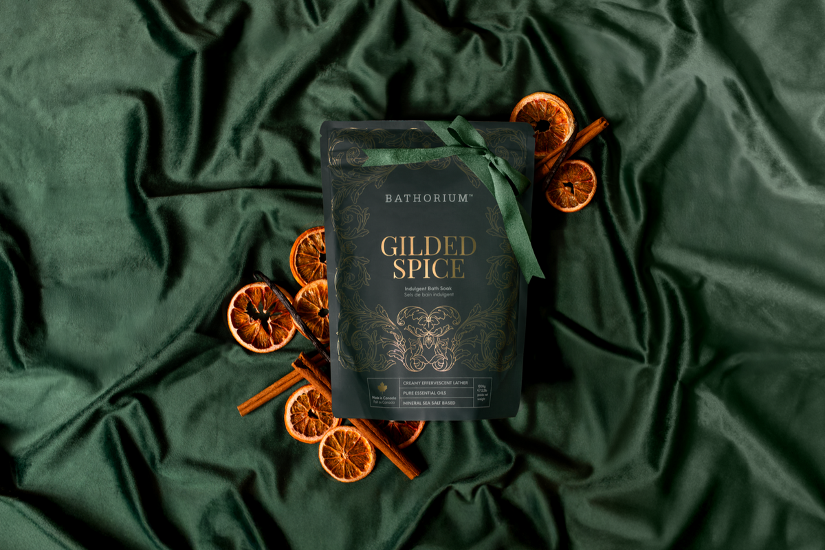 Gilded Spice Bath Soak 1 kg pouch tied with a green ribbon on green silk among dried orange slices and cinnamon