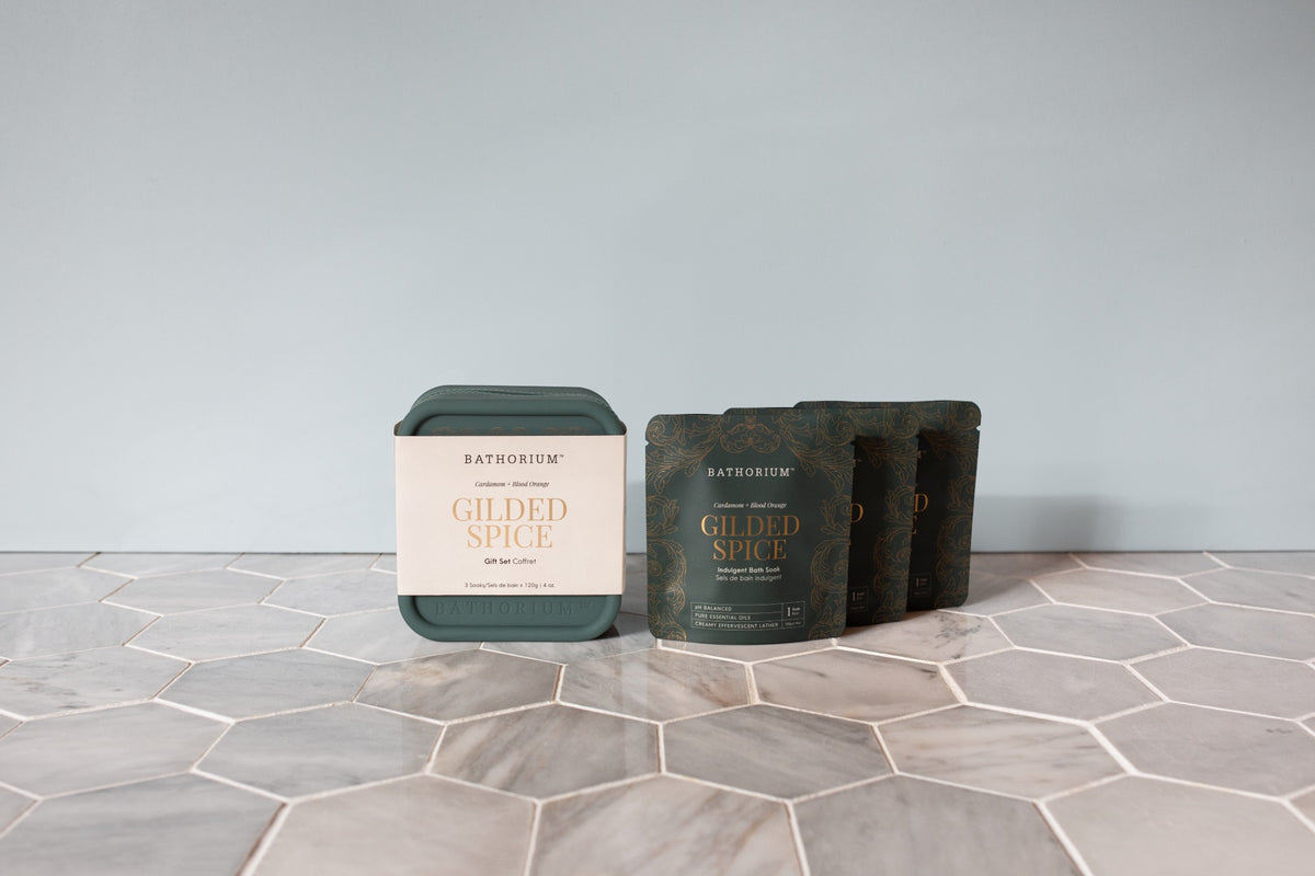 The Gilded Spice travel case beside three single Gilded Spice soak pouches on hexagon tile